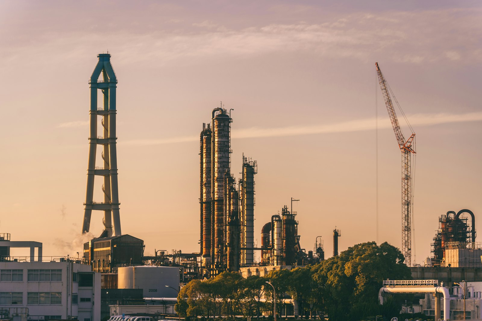 Refinery towers and a construction crane silhouetted against a dusk sky
